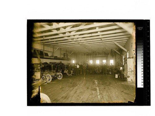 [Workers pose by autos in a service garage]