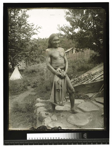 [Elderly man standing in front of a traditional house]