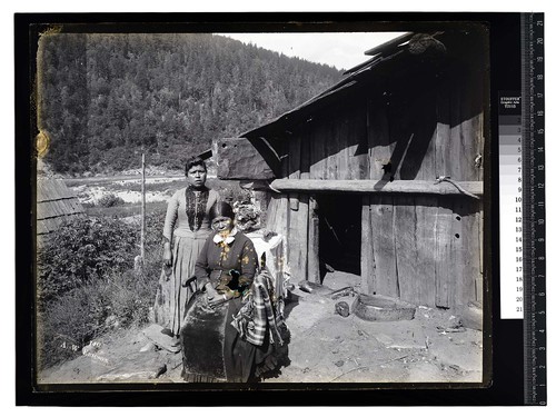 [Two Indian women pose in front of a traditional house]