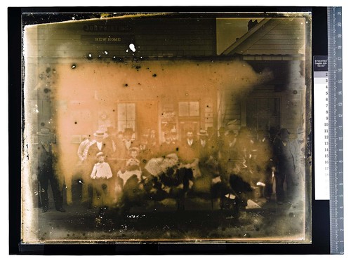 [Group posing in front of store with a mule carrying a pack]