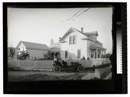 [A couple sitting in back of automobile parked beside a house]