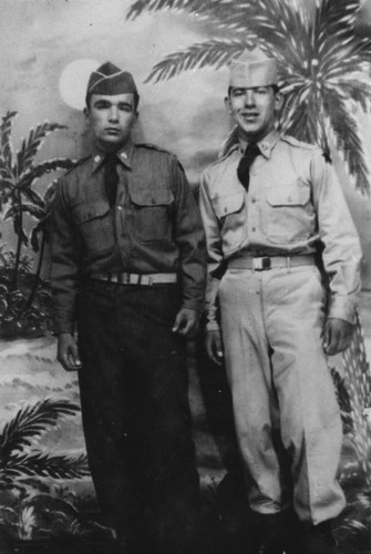 Two soldiers in uniform posed with tropical backdrop