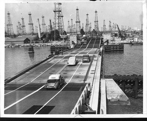 Cars crossing a bridge connecting Terminal Island to the mainland, with an oil field in the background