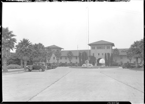 Exterior view of an unidentified Spanish-style building with a large parking lot in the foreground