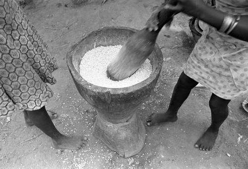 Two women standing outside grinding corn in a large pot, San Basilio de Palenque, 1977