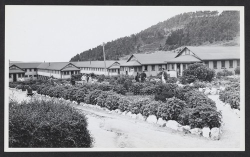 [exterior of barracks with detainees walking through gardens]