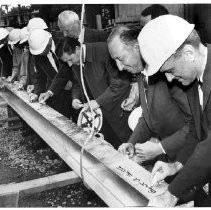 Bert A. Betts and unidentified men signing construction beam at Capitol Towers Apartments