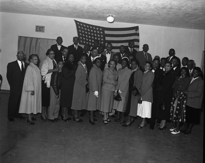 Group photograph of men and women standing in front of American flag