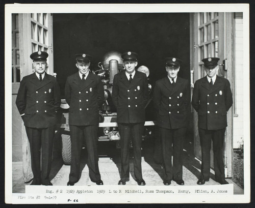 Firefighters in dress uniforms pose in front of apparatus parked in open bay at Station No. 2, 526 East Anaheim Street