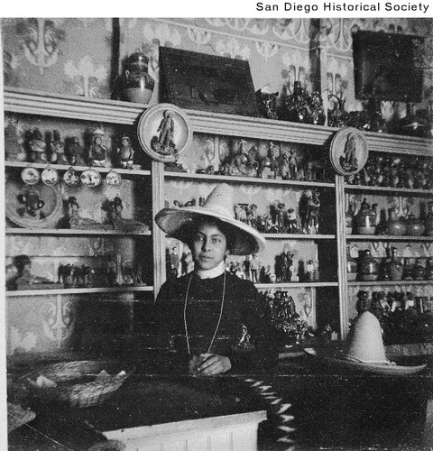 A woman wearing a hat standing in front of a wall of figurines