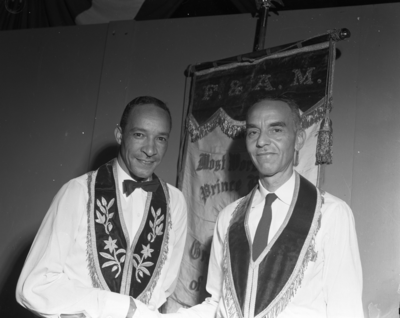 Two masons standing in front of F. & A.M. banner