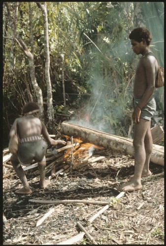 Two men heating log to remove bark