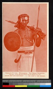Bare-chested soldier standing with spear and rifle, ca.1920-1940