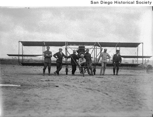 A group of men standing in front of a Curtiss biplane