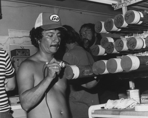 Marine technician Victor Sotelo using a heating iron to label the plastic sections of core material recovered on Leg 60 of the Deep Sea Drilling Project. The labeling was done in the Core Laboratory aboard the D/V Glomar Challenger (ship). 1978