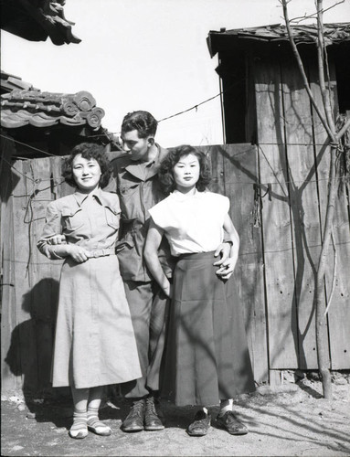 Soldier posing with two women at a Korean brothel