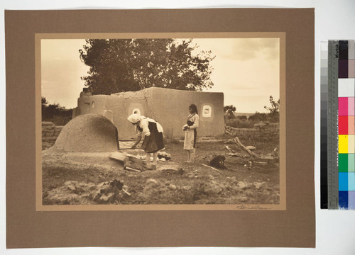 House at Summer Pueblo of Acometa, New Mexico. Mother and daughter baking bread in oven introduced by the Spaniards