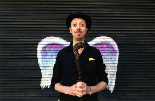 Unidentified man with a black hat and cane posing in front of a mural depicting angel wings