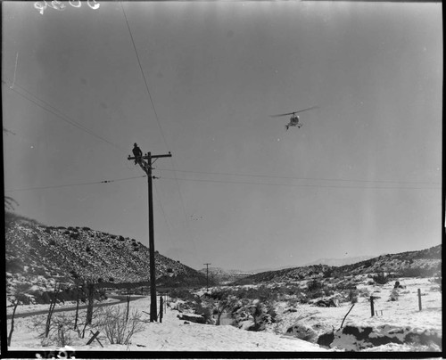 Linemen working at the top of a pole in the snow with helicopter flying near by