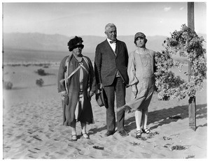 Three people posed next to a cross at a funeral in the desert