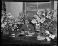 Buron Fitts sits at his desk with flowers, Los Angeles, 1927-1939
