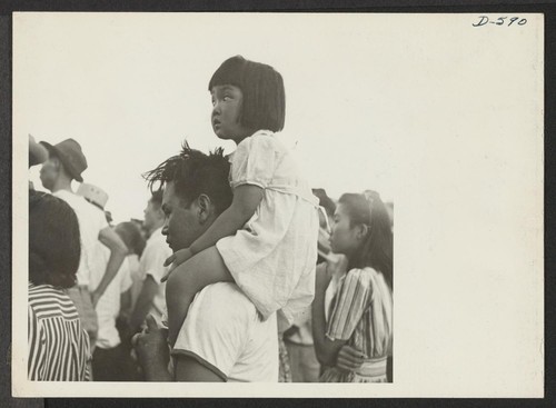 A little evacuee of Japanese descent gets a ride on her father's shoulders. Photographer: Stewart, Francis Poston, Arizona