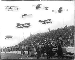 Composite photograph of early-model airplanes and a dirigible hovering above bleachers filled with spectators at the 1910 Dominguez Field Air Meet, January 1910