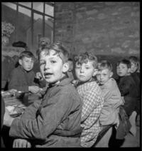 Cantine scolaire [School cafeteria. Women serving children eating at tables]