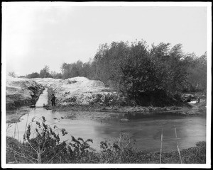 Man standing near a water ditch at the bank of Los Angeles River, north side of Griffith Park, ca.1900