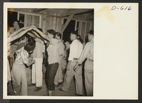 Evacuees of Japanese ancestry dance the Virginia Reel at a barn dance given by Block 12. No music was available so dancers sang pop goes the Weasel and clapped hands in time with the dance. Photographer: Stewart, Francis Poston, Arizona
