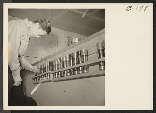 An evacuee warden inspects flashlight equipment, which is supplied to wardens for their night duty. This equipment is checked out only when wardens go on duty. Photographer: Stewart, Francis Newell, California