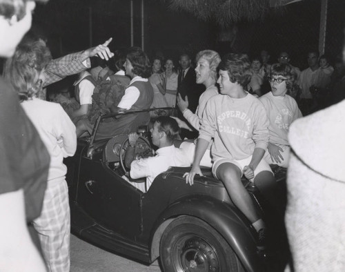 Cheerleaders riding on car during Homecoming, 1961