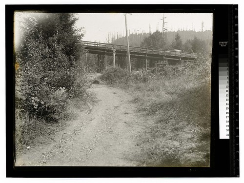 [Single lane road approaching railroad tracks and a wooden bridge]