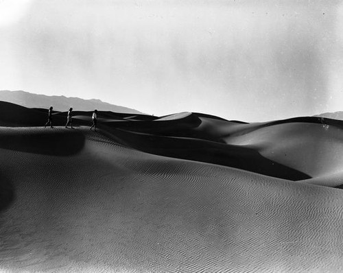 Three people walking on the sand dunes