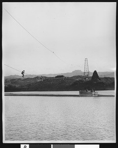 Transmission tower in background, showing employees working over a body of water, ca.1950