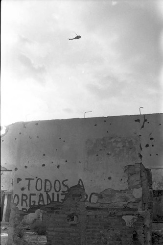 Army helicopter on patrol over a destroyed building, Perquín, 1983