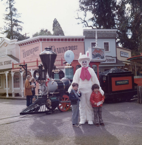 Easter Bunny poses with two children in front of Frontier Village Railroad