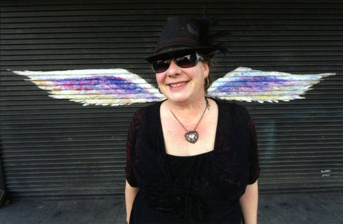 Unidentified woman in sunglasses posing in front of a mural depicting angel wings