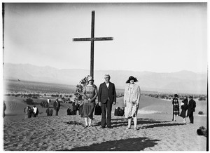 Three people standing in front of a wooden cross at a funeral in the desert