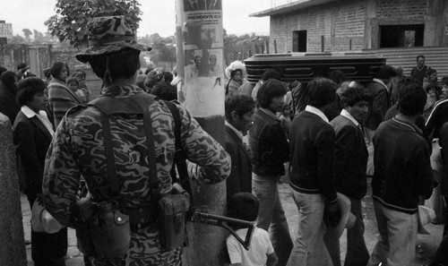 Armed soldier observes a funeral procession, Guatemala, 1982