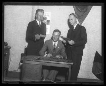Three men in suits, posing behind a desk