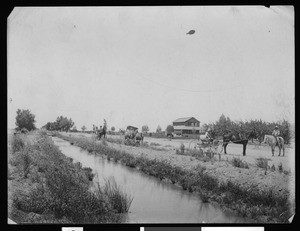 Irrigation canal and horse-drawn carriages next to a residence near Brawley, ca.1910