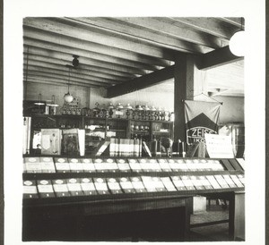 Hampankatta Laden in Mangalore, Mai 1938. Blick durch den Laden. Im Vordergrund eine Ausstellung von Büchern, die 14-täglich gewechselt wird. Im Hintergrund wieder die grossen Kästen mit Lampen usw