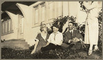 [Family seated on ground near building]