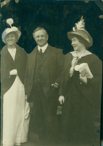 Two unidentified women standing on either side of an unidentified man