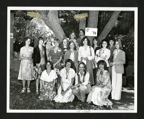 Scripps alumnae standing by a class of '74 sign nailed to a tree in Margaret Fowler Garden, Scripps College