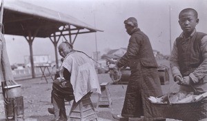 Itinerant barber cutting man's hair. Wuhan, China, 1911