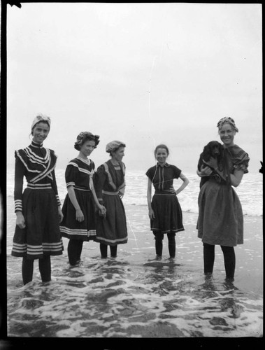 A group of five young women standing in the water at the beach