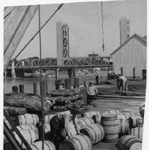 Workers rolling barrels on Sacramento pier with Tower Bridge in the background