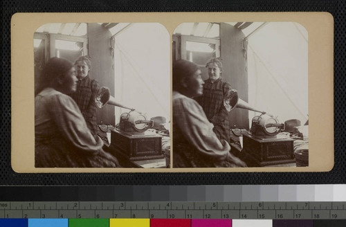 Ramona Lubo speaking into George Wharton James' graphophone, inside his wagon. Behind her is Mary Noble, a teacher at the Soboba Indian School